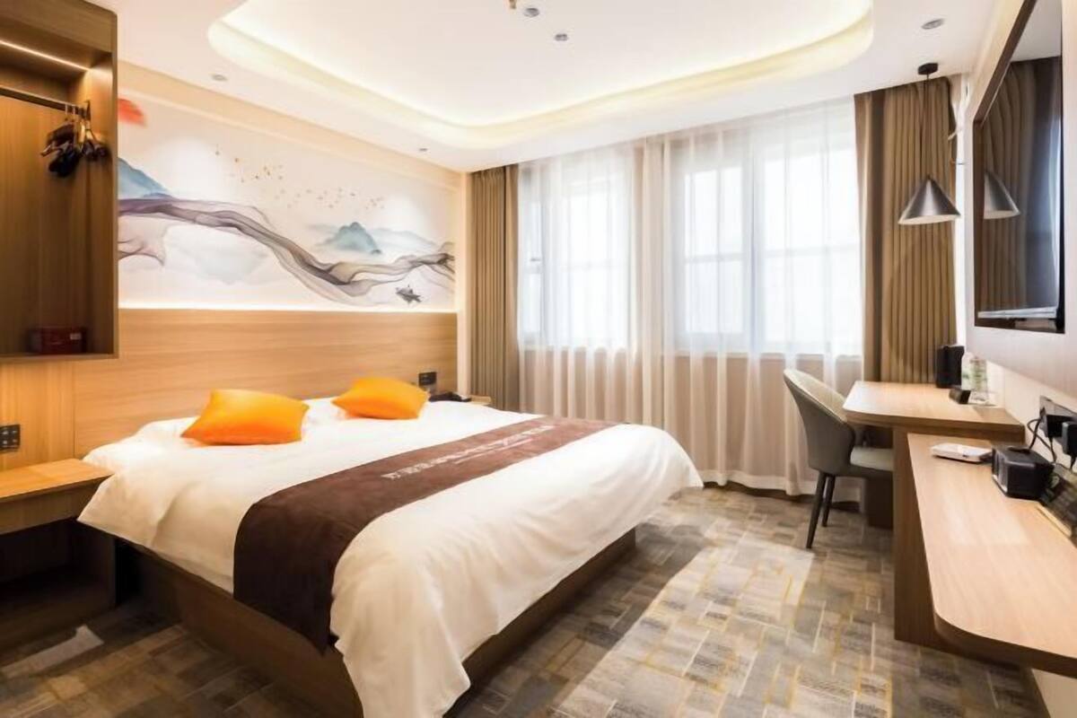 Habitación de hotel con cama, escritorio y un ventanal con cortinas.