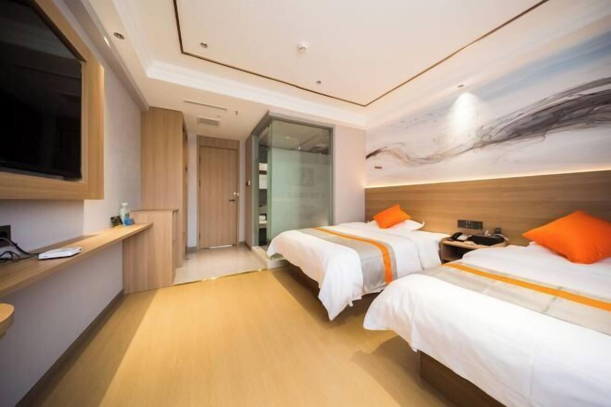 Habitación de hotel con dos camas, un escritorio, un televisor y un cuadro en la pared.