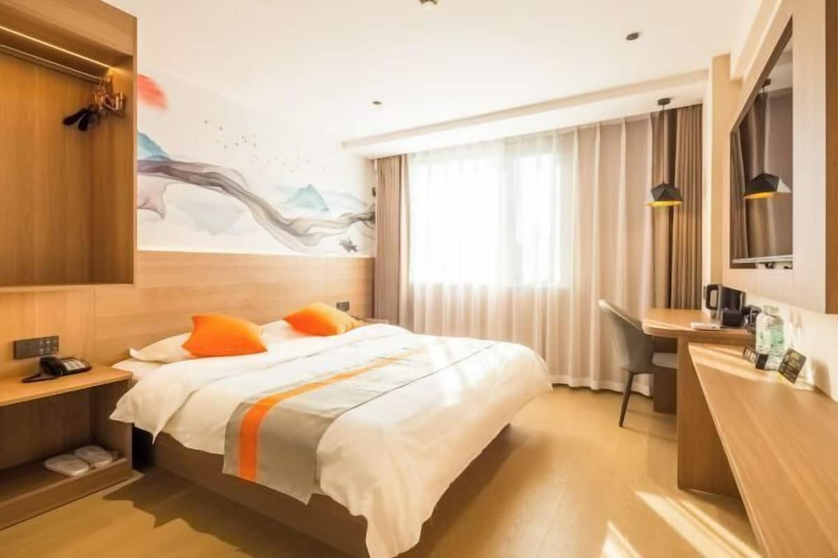 Habitación de hotel con cama, mesita de noche, escritorio, silla y un amplio ventanal con cortinas.