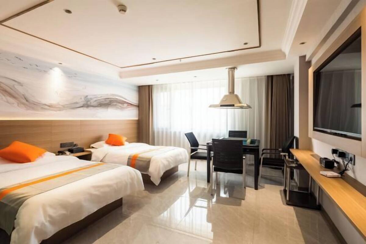 Habitación de hotel con dos camas, un escritorio, una silla, un televisor y un ventanal con cortinas.