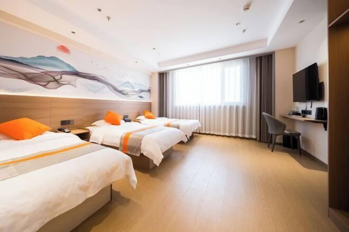 Habitación de hotel con tres camas, un televisor de pantalla plana, un escritorio y un ventanal con cortinas.