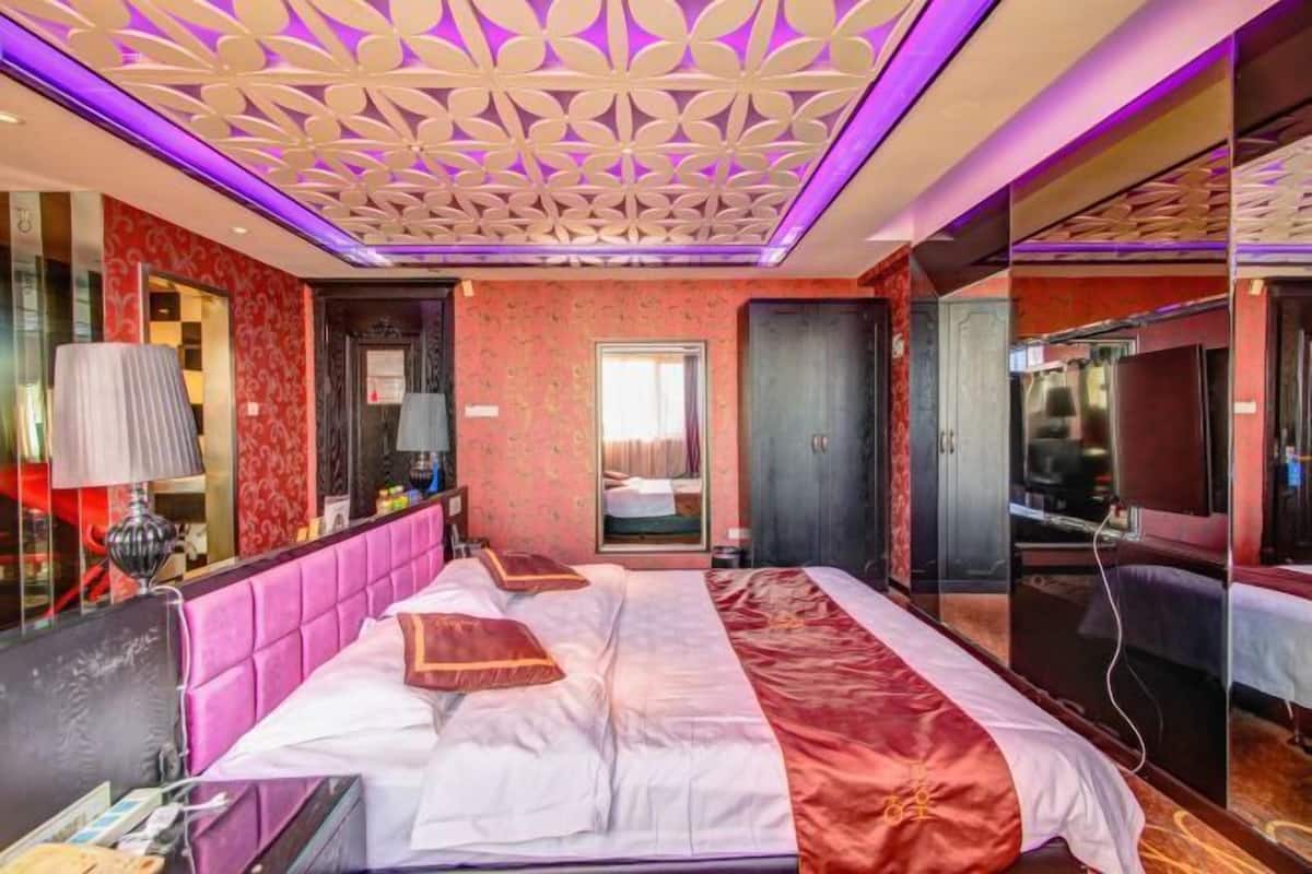A hotel room with a large bed, a mirror, a vanity, and a bathroom visible through a glass partition.