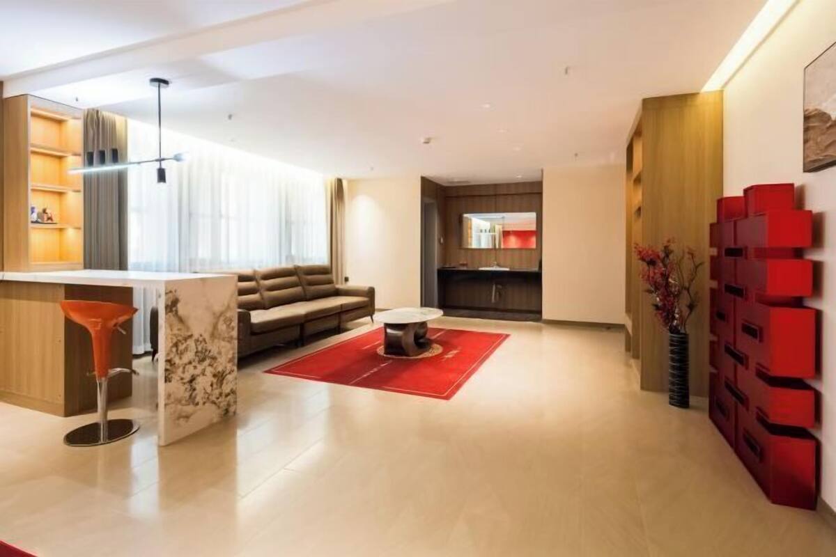 Una sala de estar moderna con un sofá, una mesa de centro, una alfombra roja y una cocina con mostrador y armarios.