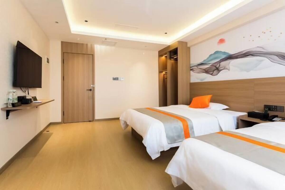 Habitación de hotel con dos camas, televisor, un cuadro en la pared y una puerta de madera.