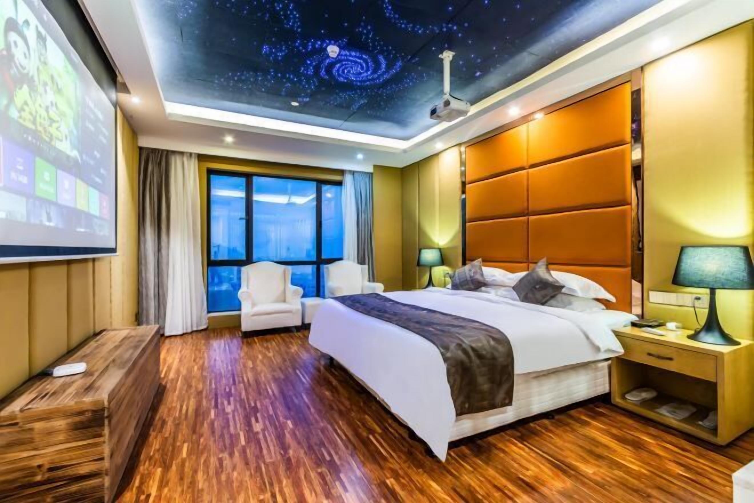 Ein Hotelzimmer mit Sternenhimmel, einem großen Bett, einer Sitzecke mit Bildschirm und Blick ins Freie.