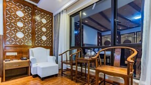 Una habitación con piso de madera, un sillón blanco, una mesa de madera con sillas, un separador de madera con un diseño geométrico y un ventanal con vistas al exterior.