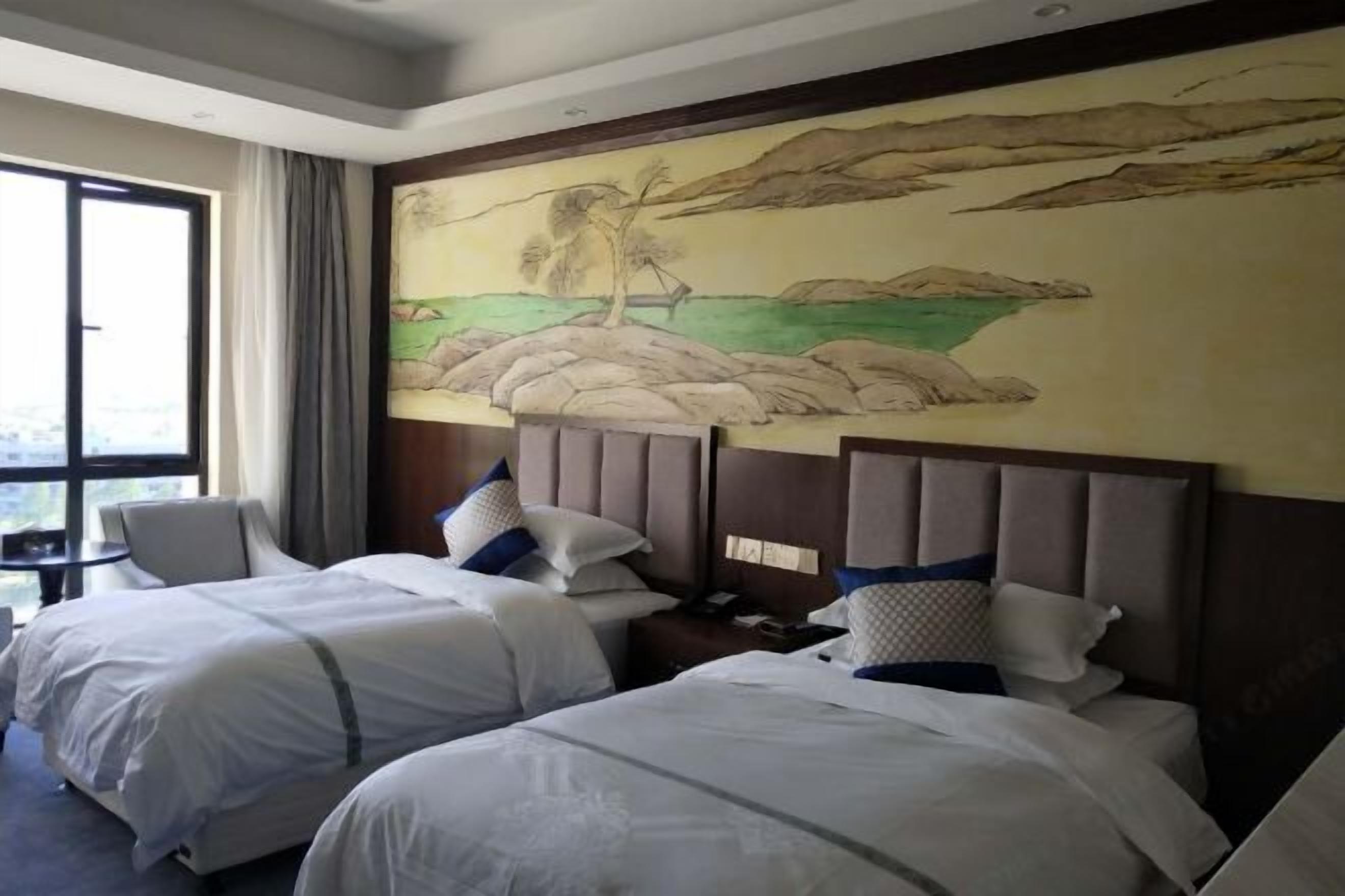 A hotel room with two beds, a large window, and a mural of a landscape on the wall.