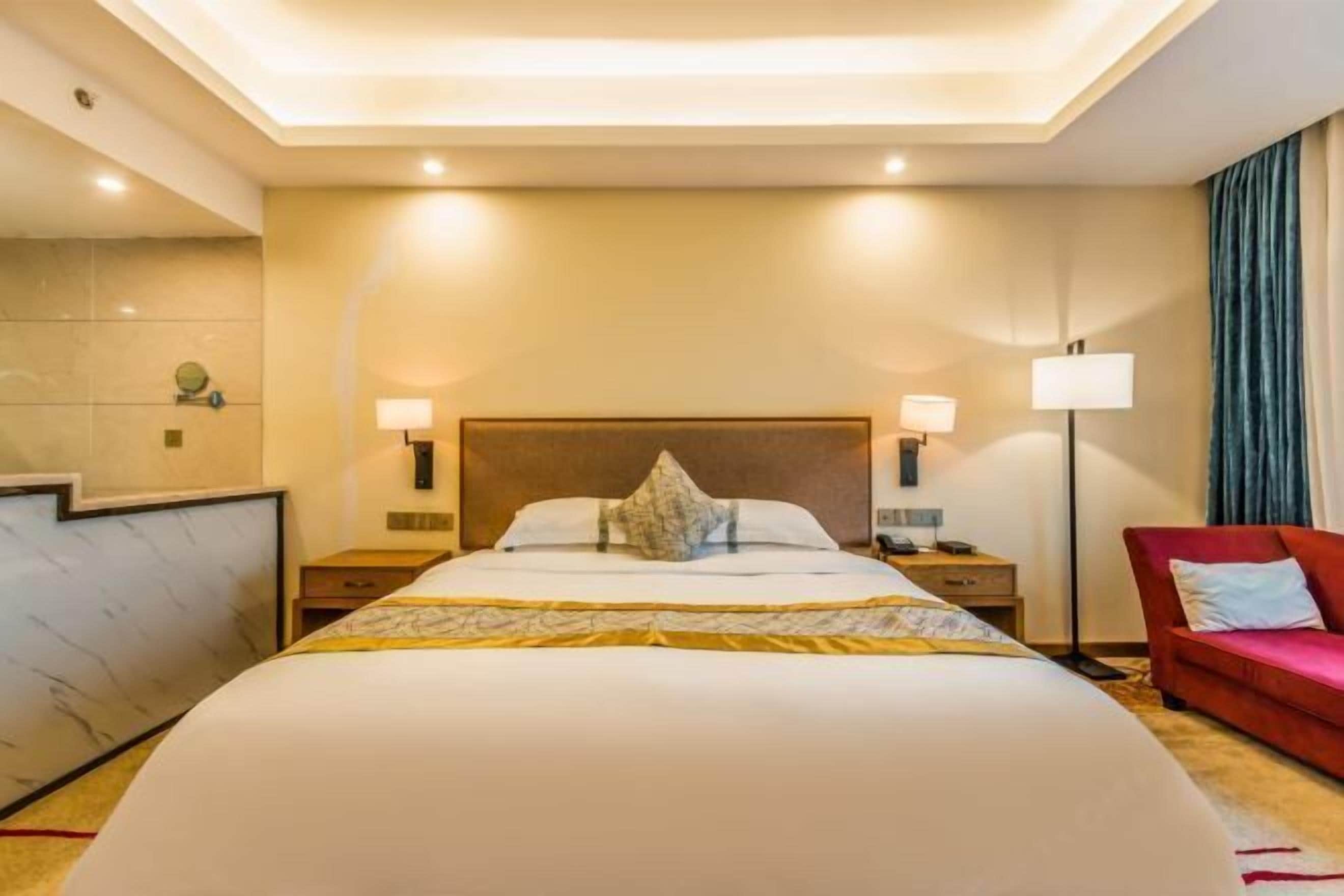 A hotel room with a large bed, two bedside tables, a red sofa, and a floor lamp.