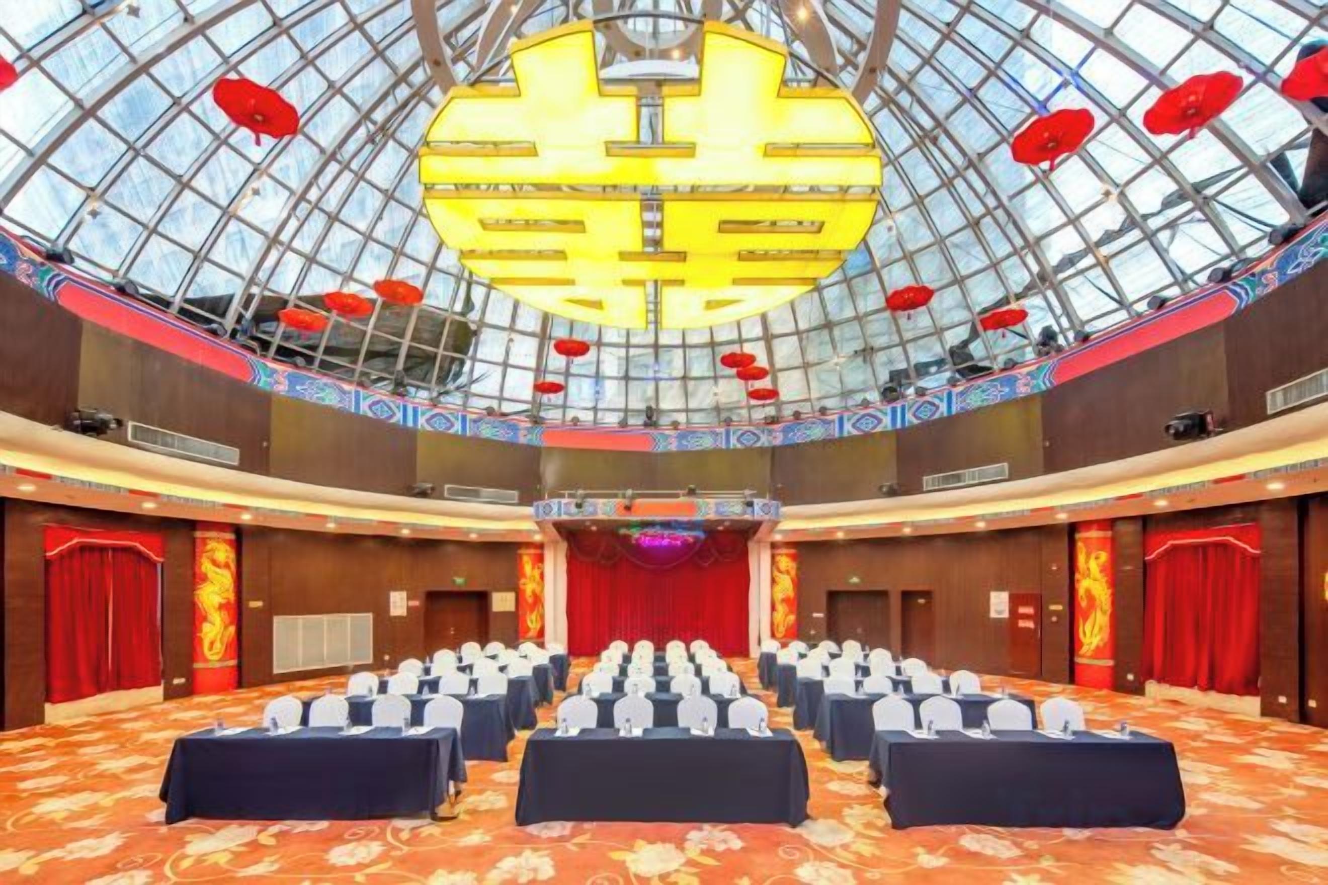 A conference room with rows of tables and chairs, a large chandelier, and a glass ceiling.