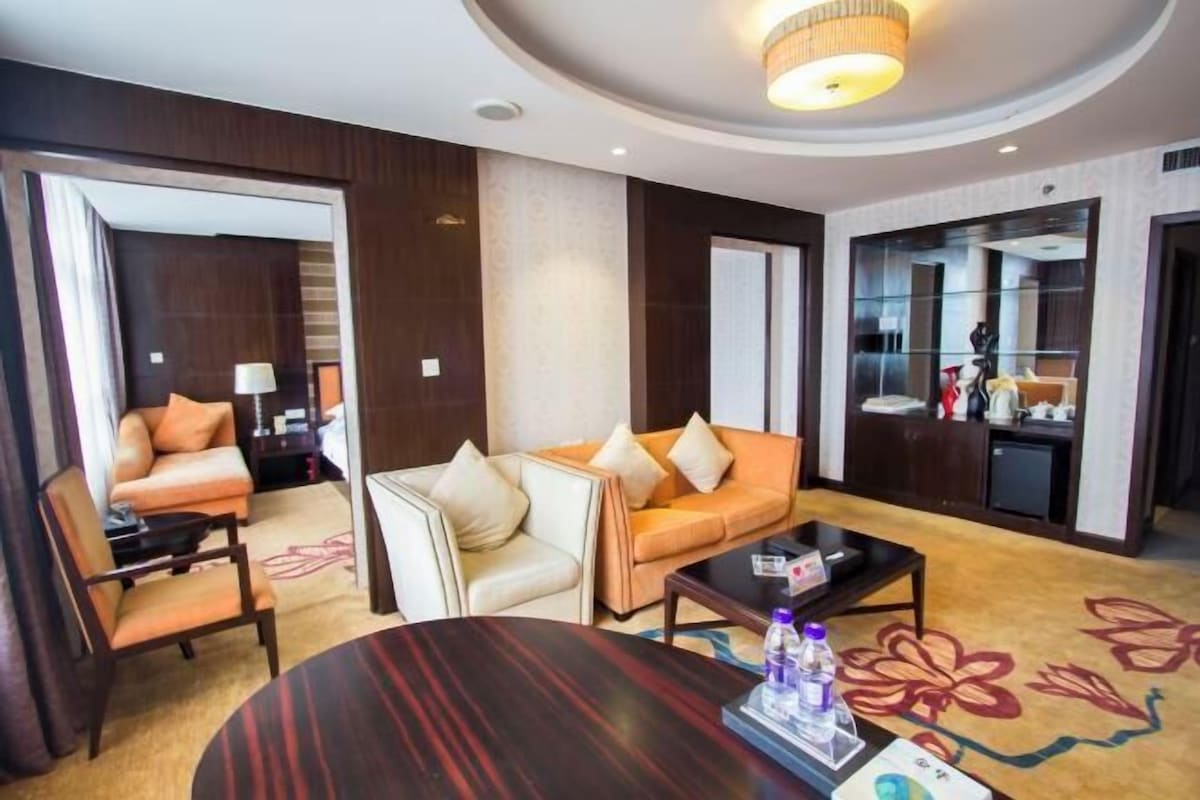 A hotel room with a round table, two sofas, a small coffee table, and a mirror.