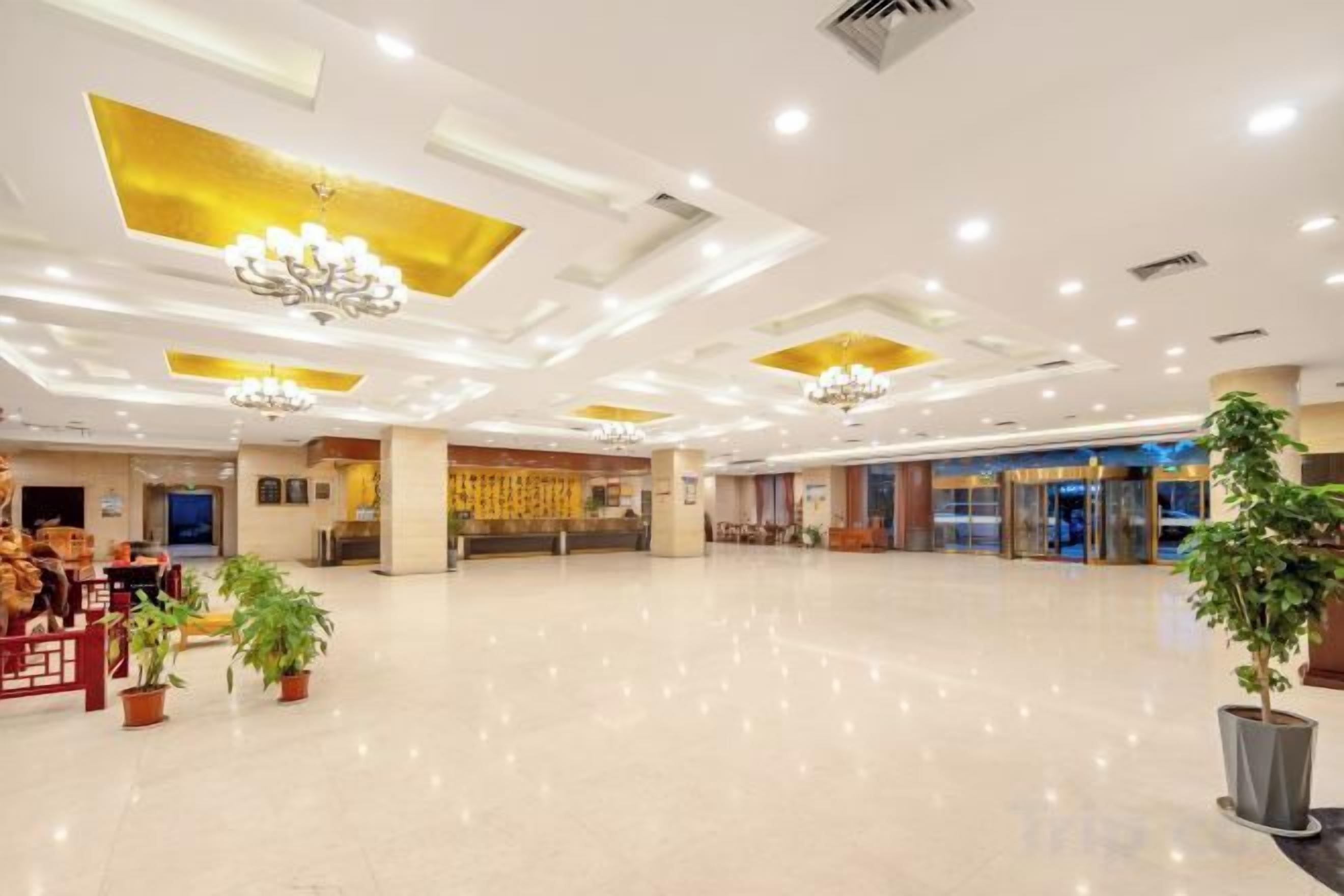 A spacious lobby with a polished floor, chandeliers, and potted plants.
