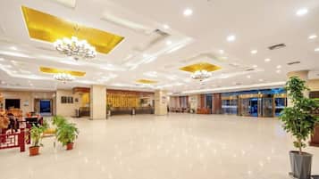 A spacious lobby with a polished floor, chandeliers, and potted plants.