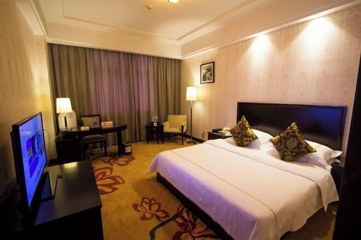 A hotel room with a large bed, a desk with a computer, a chair, and a TV.