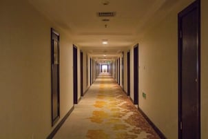 Corredor comprido e estreito de um hotel, com portas em ambos os lados e carpete estampado.