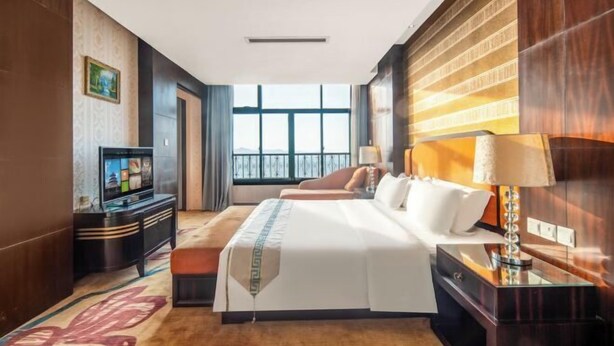 A hotel room with a large bed, a TV, a desk, and a window with a view. - Mingzhao Hot Spring International Hotel (Wuyi)