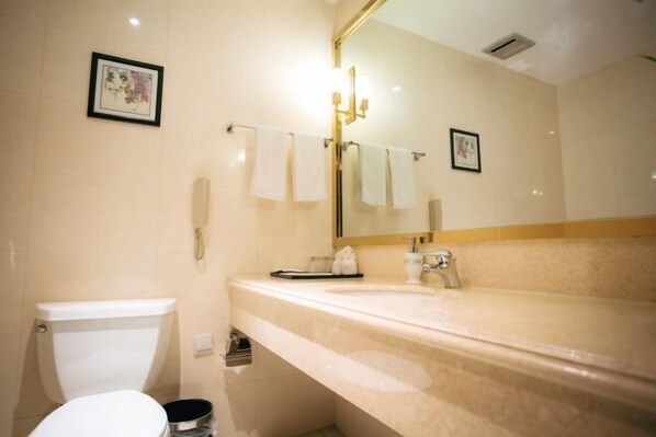 A bathroom with a toilet, sink, and mirror. There are towels hanging on a rack and a framed picture on the wall.
