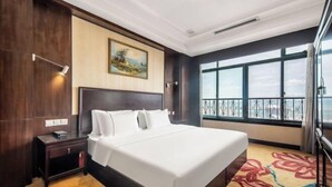 A hotel room with a large bed, a nightstand, a painting on the wall, and a window with a view. - Mingzhao Hot Spring International Hotel (Wuyi)