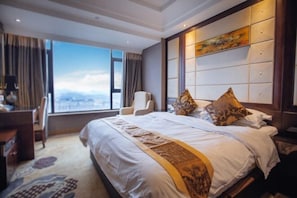 A hotel room with a large bed, a desk, and a chair. There is a window with a view of the city. - Mingzhao Hot Spring International Hotel (Wuyi)