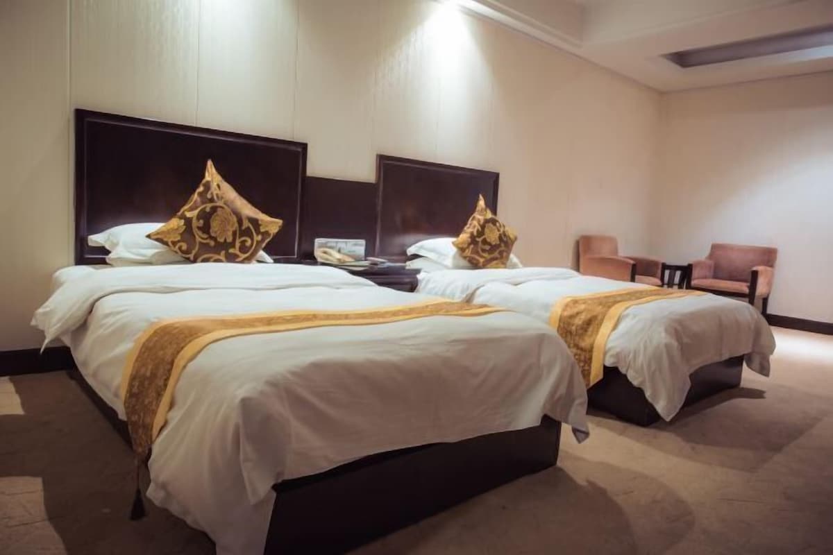 A hotel room with two beds, each with a headboard, a small table, and a chair.