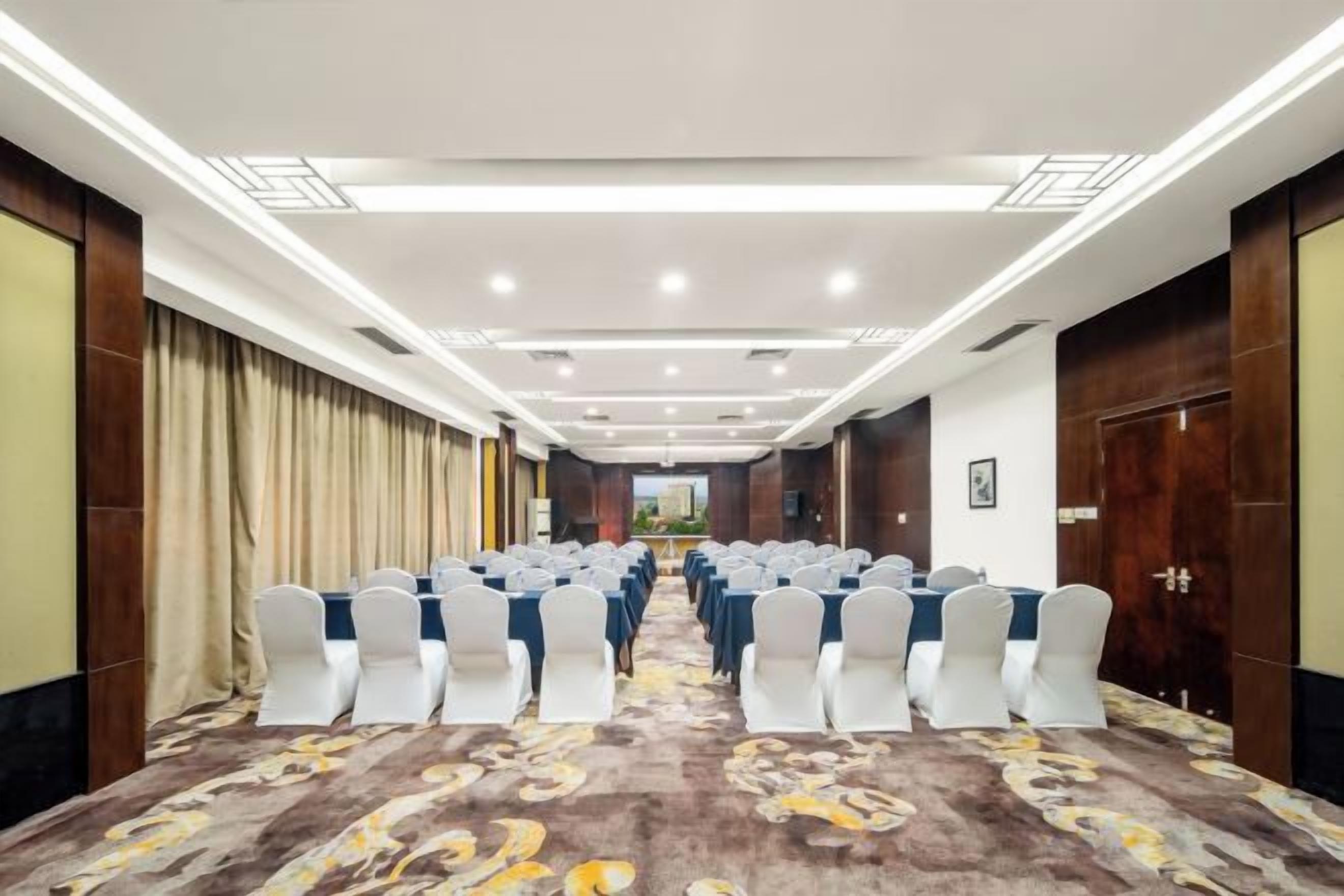 A conference room with rows of white chairs, a carpeted floor, and a long table.