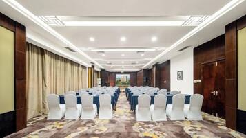 A conference room with rows of white chairs, a carpeted floor, and a long table.