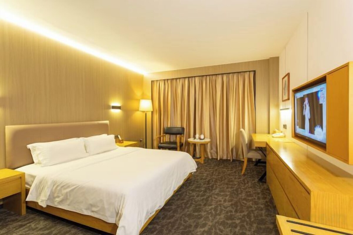 A hotel room with a bed, a desk, a chair, a TV, and a window with curtains.