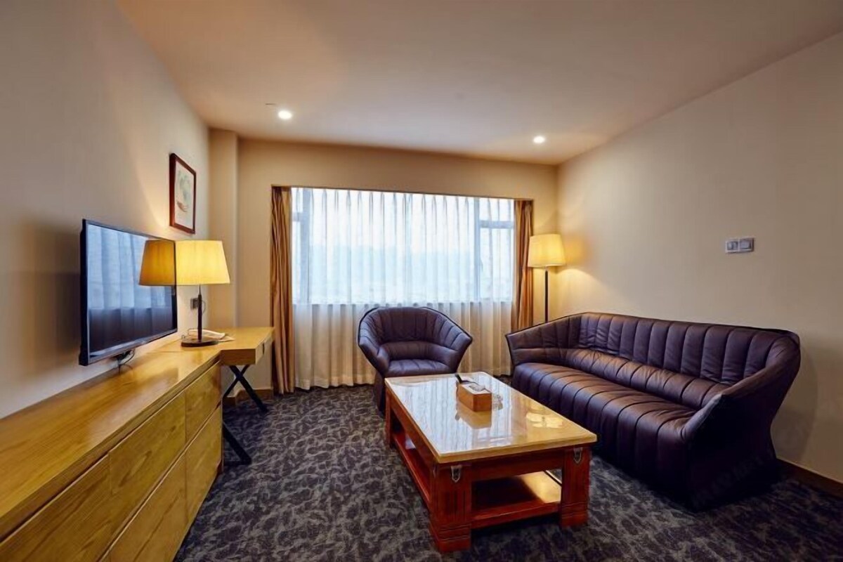 A hotel room with a television, a sofa, a chair, a table, and a window with curtains.