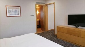 A hotel room with a bed, a television, a dresser, a framed picture on the wall, and an open door leading to a bathroom. - Xiya Hotel (Foshan)