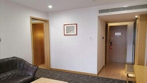 A room with a black leather sofa, a wooden table, a framed picture on the wall, and a door leading to another room. - Xiya Hotel (Foshan)