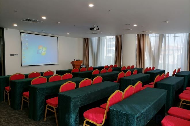 A conference room with rows of tables and chairs, a projector screen, and a podium.