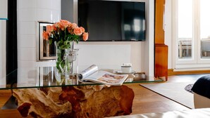 Ein modernes Wohnzimmer mit einem Glastisch, einer Blumenvase, einer Zeitschrift und einem Fernseher an der Wand.