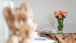 Eine transparente Glasvase mit rosa Rosen auf einem Glastisch, eine transparente Teekanne und eine Zeitschrift.