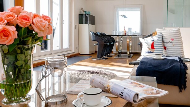 Ein modernes Wohnzimmer mit einem Glastisch, einem Blumenstrauß und einem Sofa mit gestreiften Kissen.
