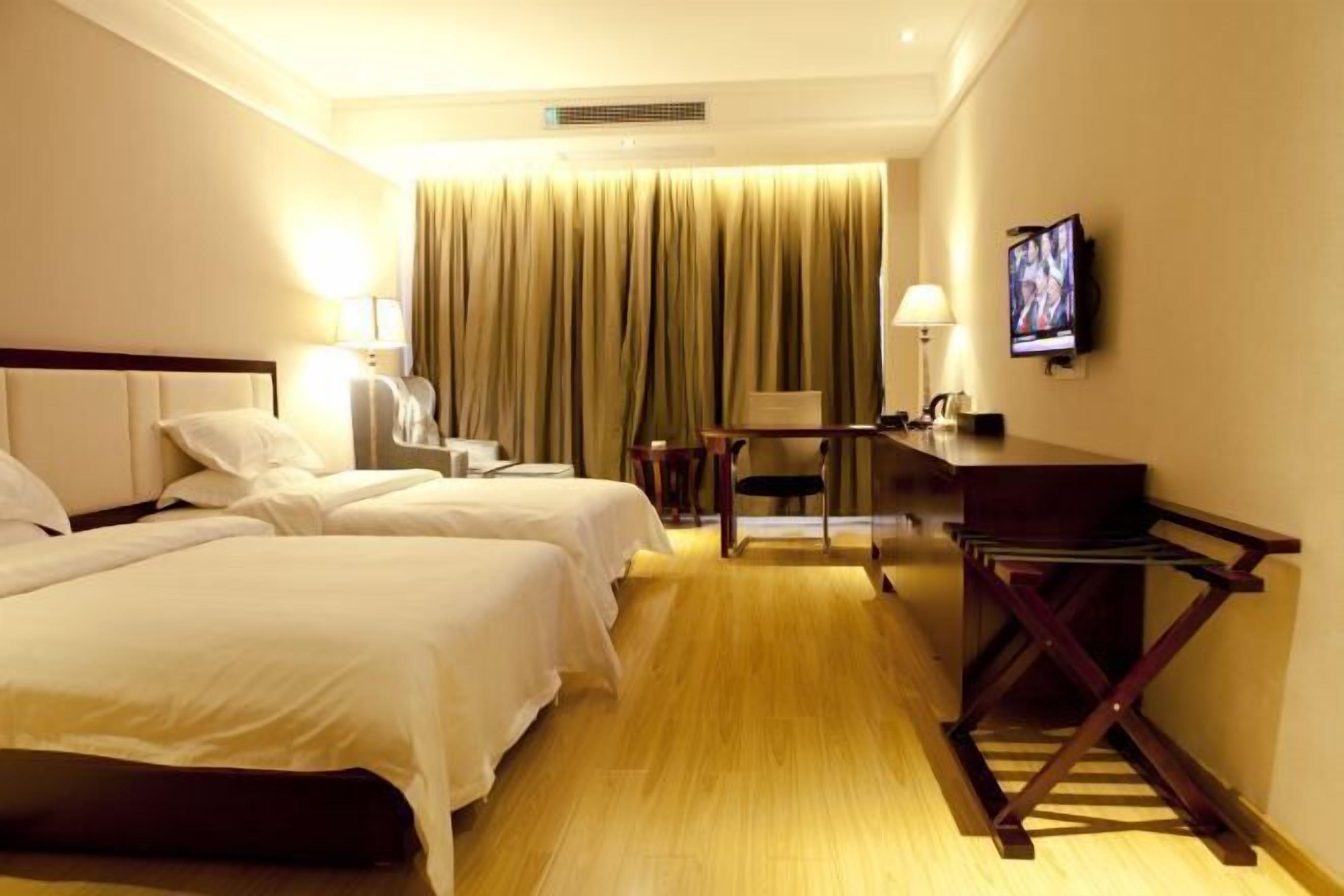 A hotel room with two beds, a desk, a chair, a TV, and a curtain.