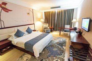 A hotel room with a large bed, a desk, a chair, a TV, and a window with curtains. - Haiyue Junlan Hotel (Huangshan City)