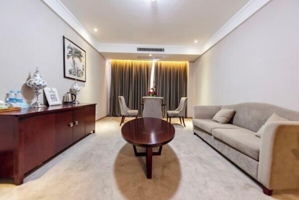Una habitación de hotel moderna con una mesa de centro redonda de madera, un sofá, una mesa de comedor con sillas y un armario.