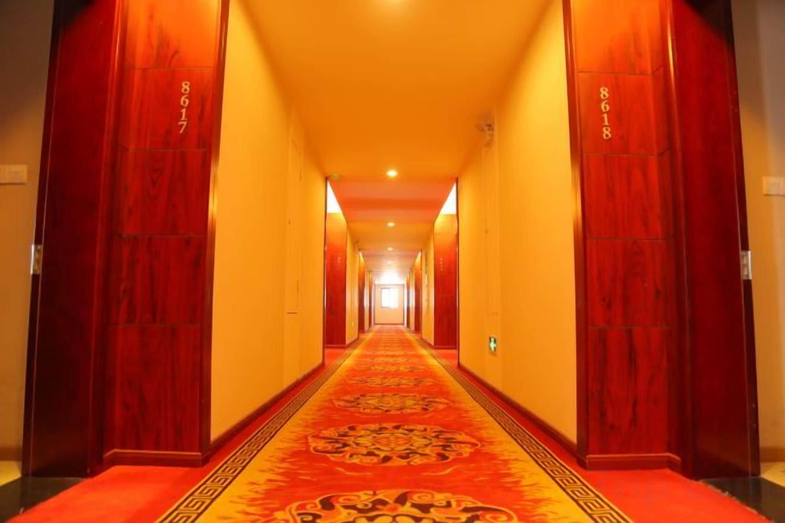 A hotel hallway with a red carpet, wooden doors, and a patterned carpet runner.