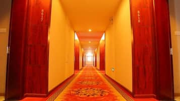 A hotel hallway with a red carpet, wooden doors, and a patterned carpet runner.
