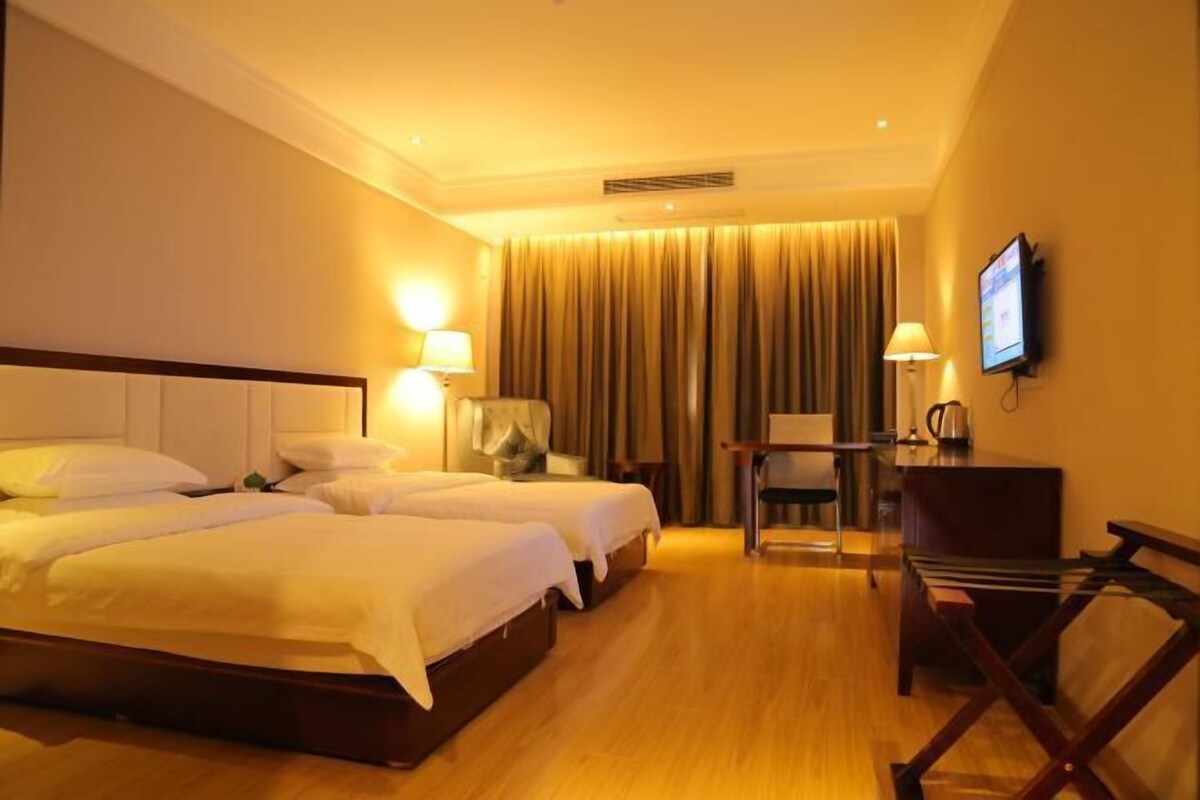 A hotel room with two beds, a desk, a chair, a television, and a window with curtains.