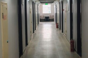 A long, narrow hallway with doors on both sides, fire extinguishers, and a fire alarm on the right wall. - Sunshine Hotel (Yuncheng Wanda Plaza Central Hospital) (Yuncheng)