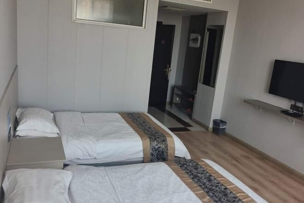 A hotel room with two beds, a television on the wall, and a hallway leading to another room.