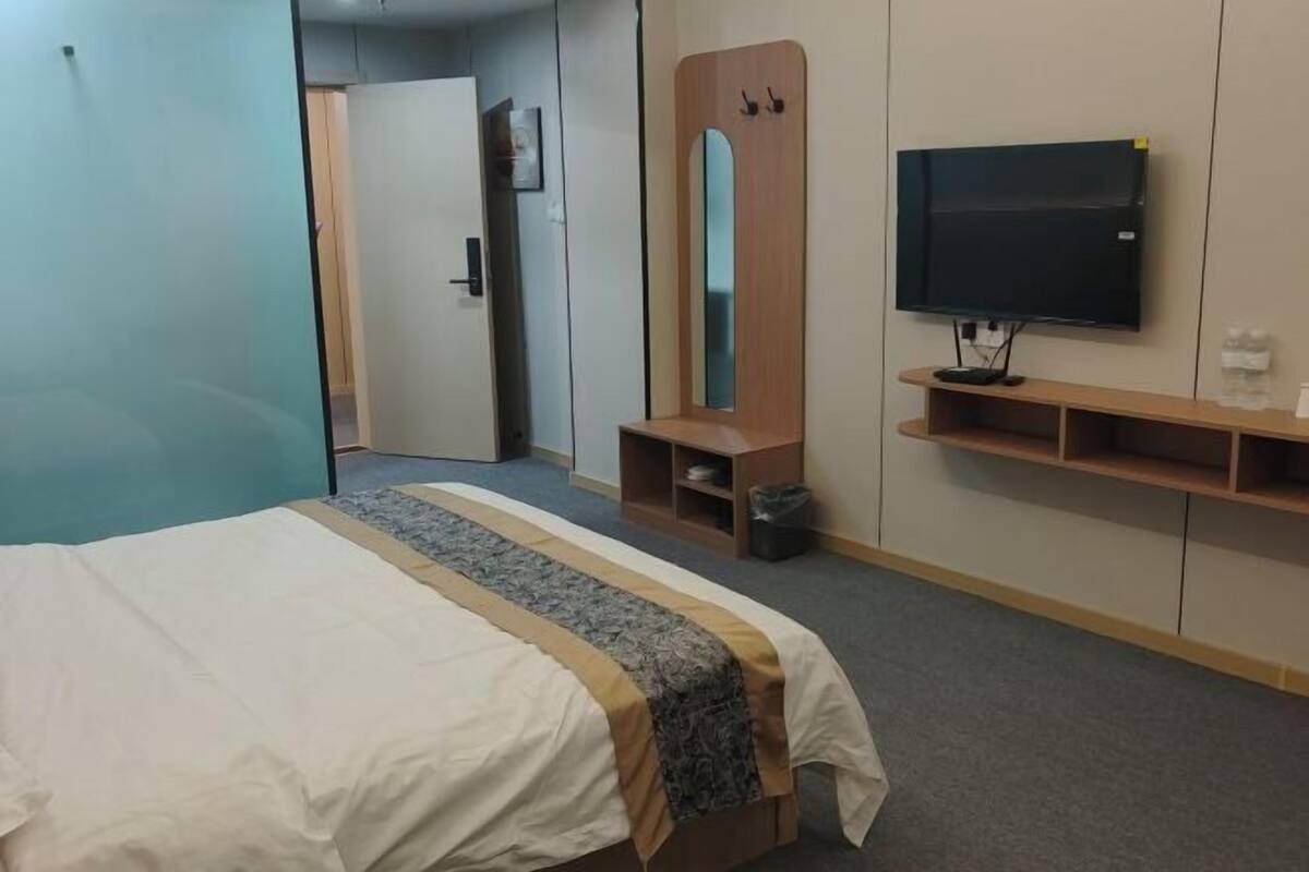 A hotel room with a bed, a television, a mirror, and a wardrobe.