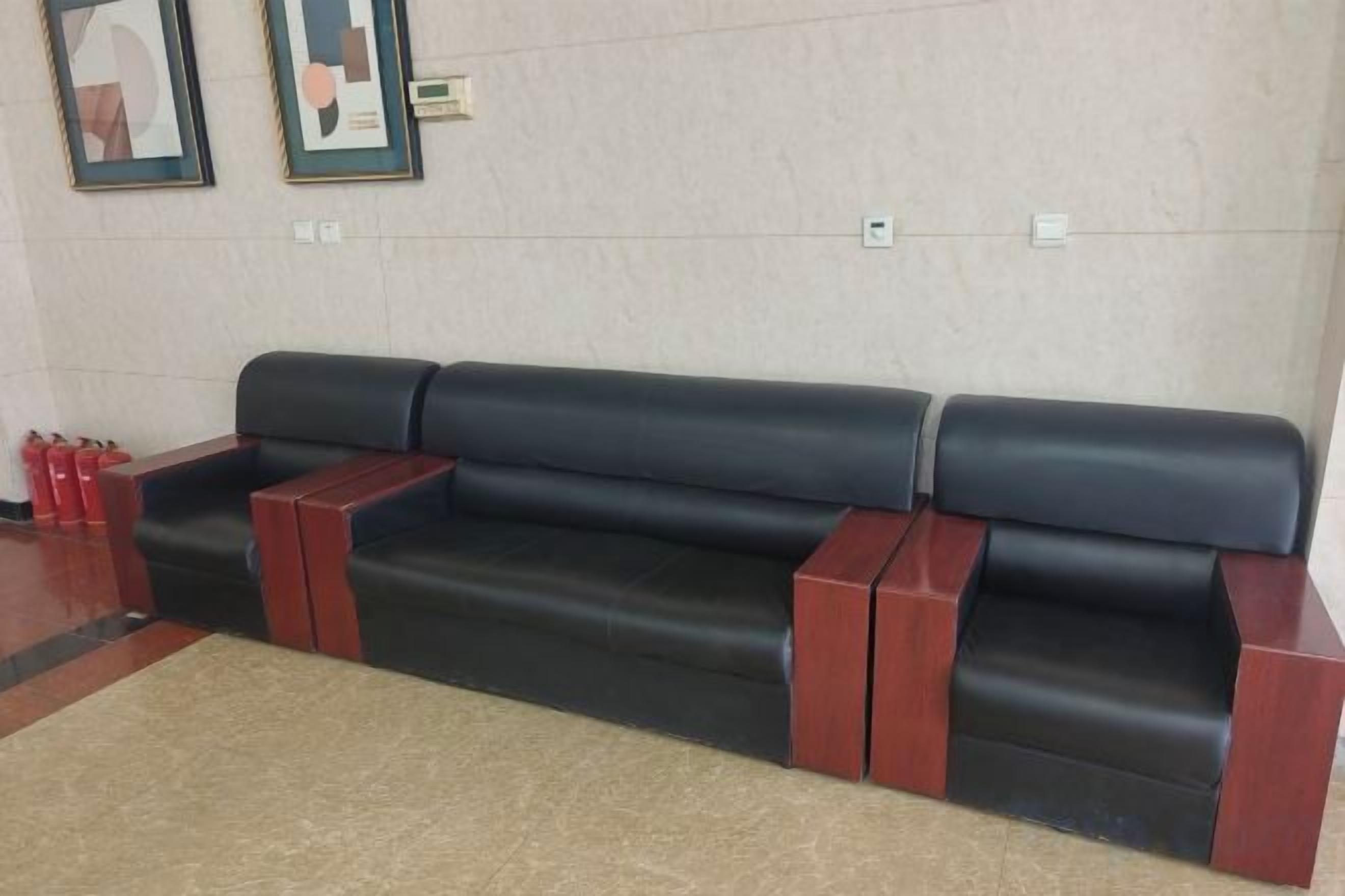 A black leather sofa with wooden armrests and a beige rug in a lobby area.