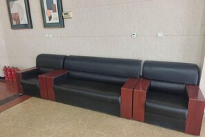A black leather sofa with wooden armrests and a beige rug in a lobby area. - Sunshine Hotel (Yuncheng Wanda Plaza Central Hospital) (Yuncheng)