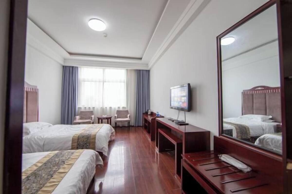 A hotel room with two beds, a television, a desk, and a large mirror.