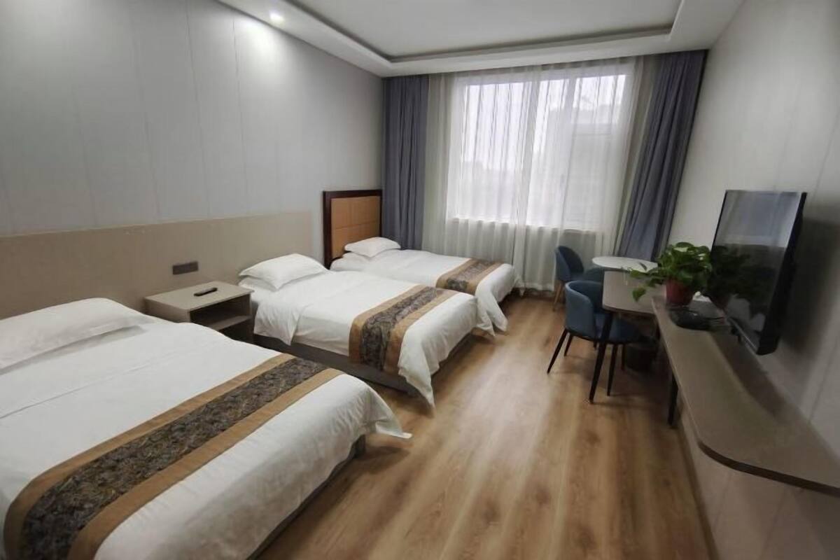 A hotel room with two beds, a desk with a chair, a TV, and a window with curtains.