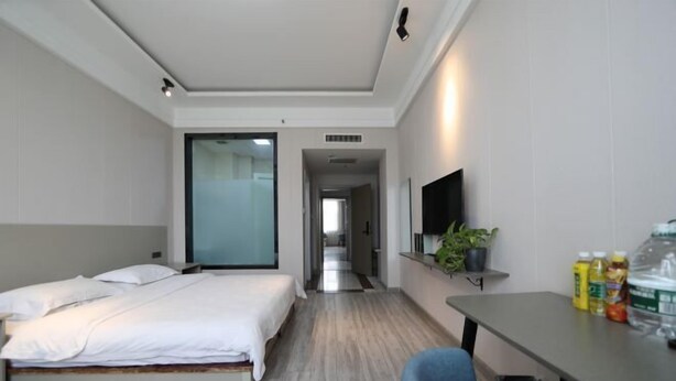 A hotel room with a bed, a desk, a chair, a TV, a plant, and a trash bin. - Sunshine Hotel (Yuncheng Wanda Plaza Central Hospital) (Yuncheng)