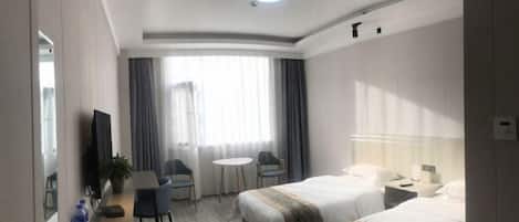 A hotel room with two beds, a desk, a chair, a small table, a TV, and a window with curtains.