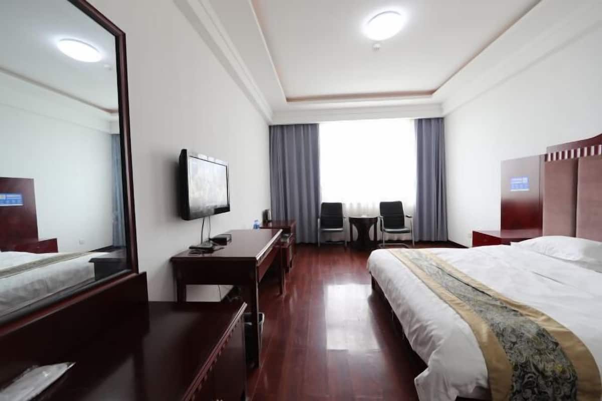 A hotel room with a bed, a desk, a chair, a television, and a window with curtains.