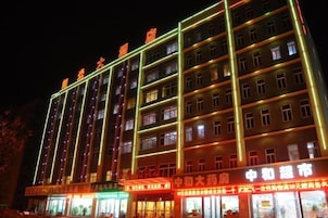 Un hotel de varios pisos con letreros iluminados y numerosas plantas.
